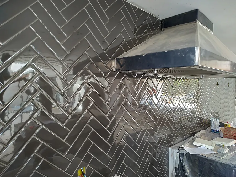 Parede de cozinha com revestimento metalizado em chevron e coifa