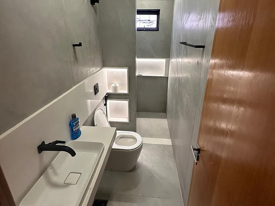 Banheiro em cimento queimado com nicho iluminado e metais pretos